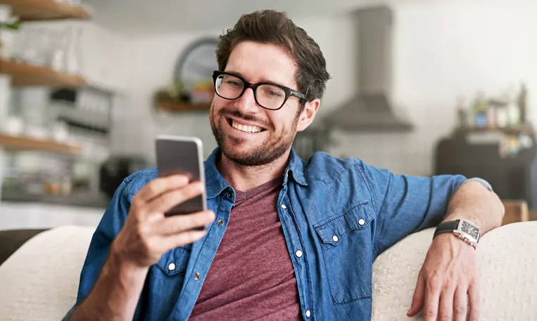 Uśmiechnięty mężczyzna w okularach korekcyjnych patrzący na telefon